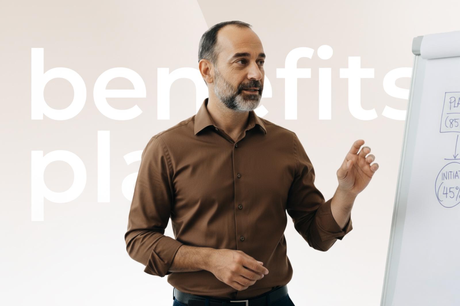 Man in a brown shirt presenting at a whiteboard with diagrams, standing in front of large text partially reading "benefits plan."