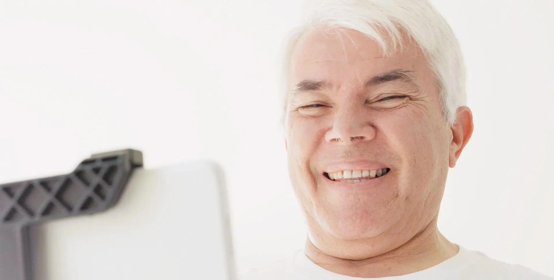Smiling older man with white hair looking at a tablet, set against a bright, white background.