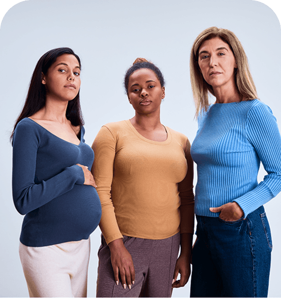 Three women stand together against a light background, each wearing a different colored long-sleeve top, looking confidently at the camera.